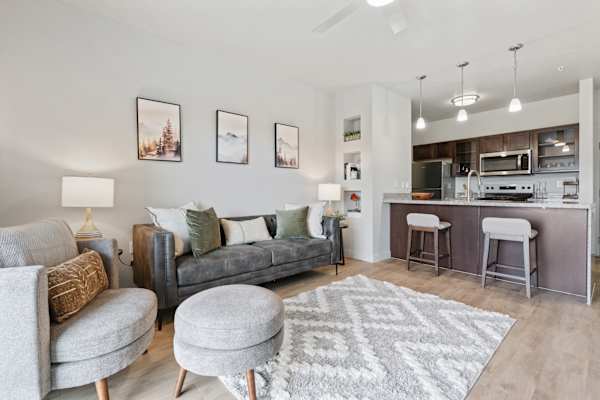 A modern living room with a grey couch, a grey ottoman, and a grey rug. at Wilmington Flats Apartments, Salt Lake City, UT, 84106